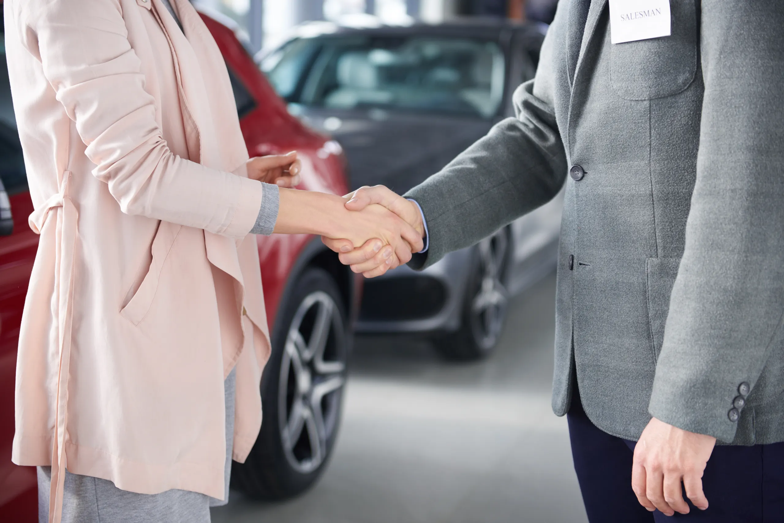 Duas pessoas apertam as mãos, um carro vermelho e um carro cinzento podem ser vistos atrás.